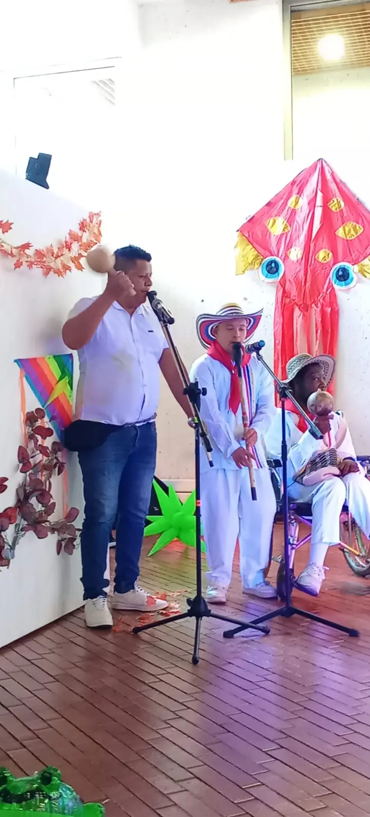 Profesor cantando con maraca junto a jóvenes que tocan la gaita y la maraca en tarima