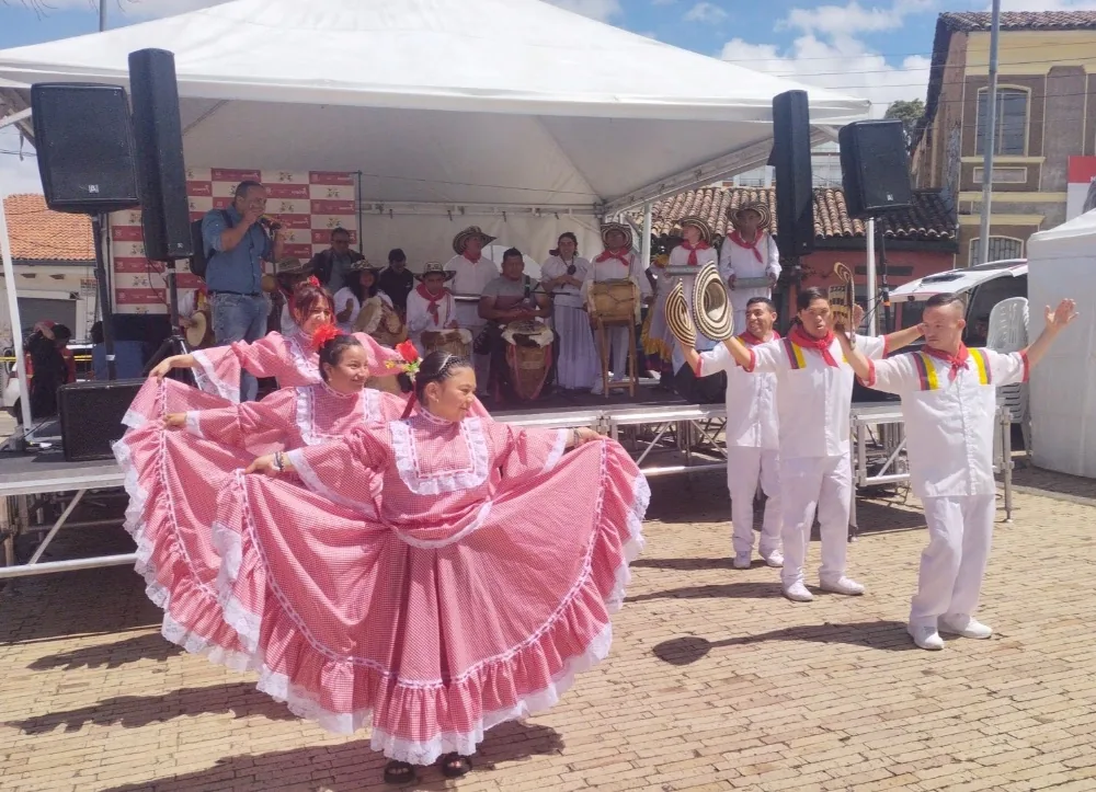 Dos jóvenes con polleras rosadas abiertas bailando en una tarima, junto a compañeros con vestuario blanco