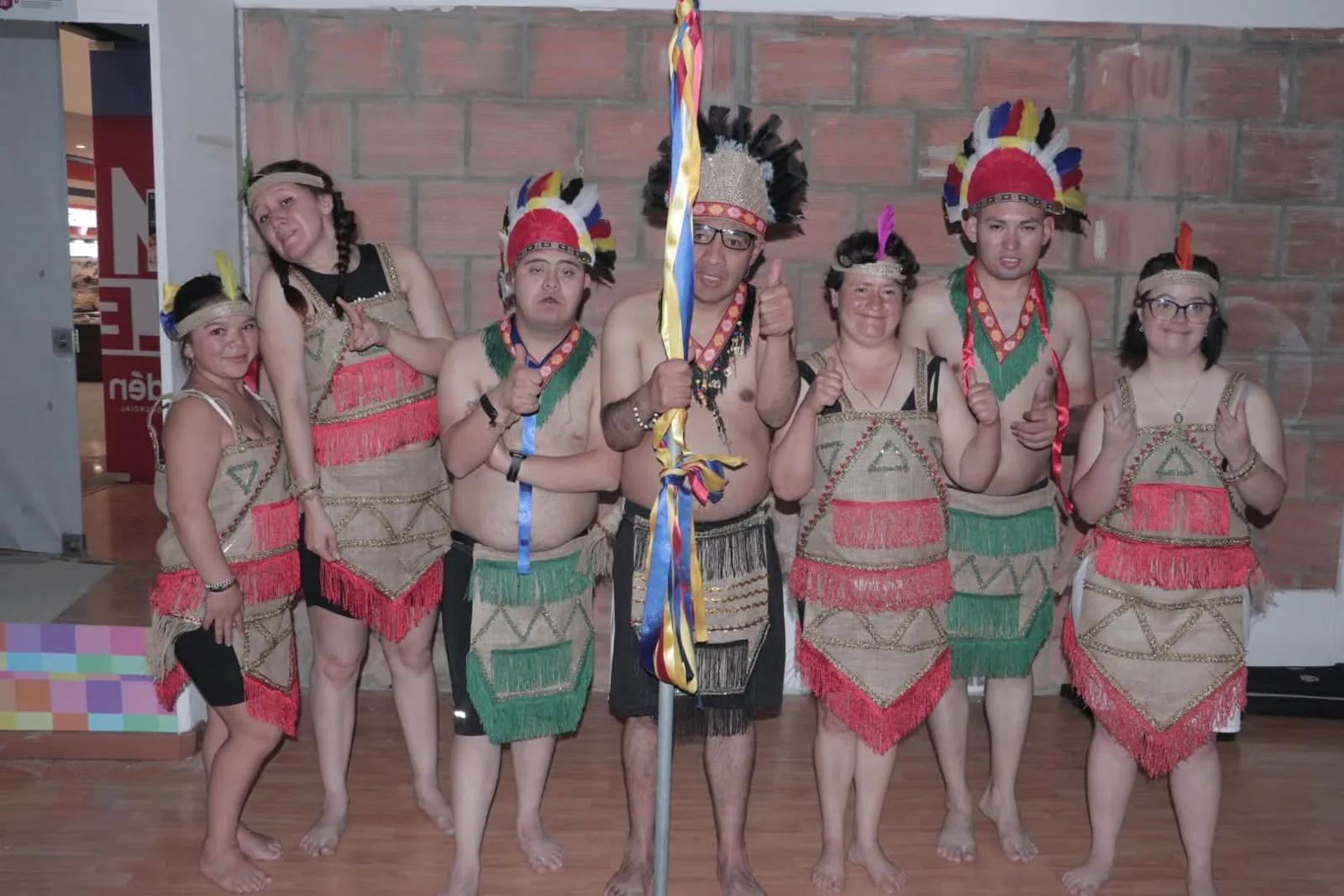 Jóvenes con trajes y penachos de colores posando antes de una presentación de danza