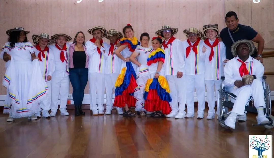 Jóvenes del grupo con vestuario blanco, pañoleta roja y polleras de colores posando en un salón