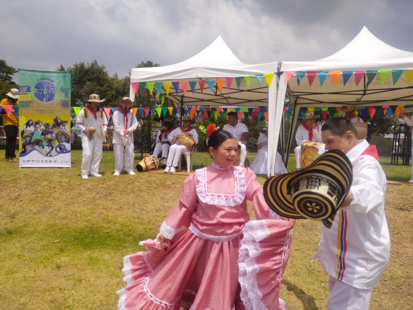 Pareja de baile con pollera rosada y sombrero vueltiao en un encuentro al aire libre, con el grupo de gaitas detrás