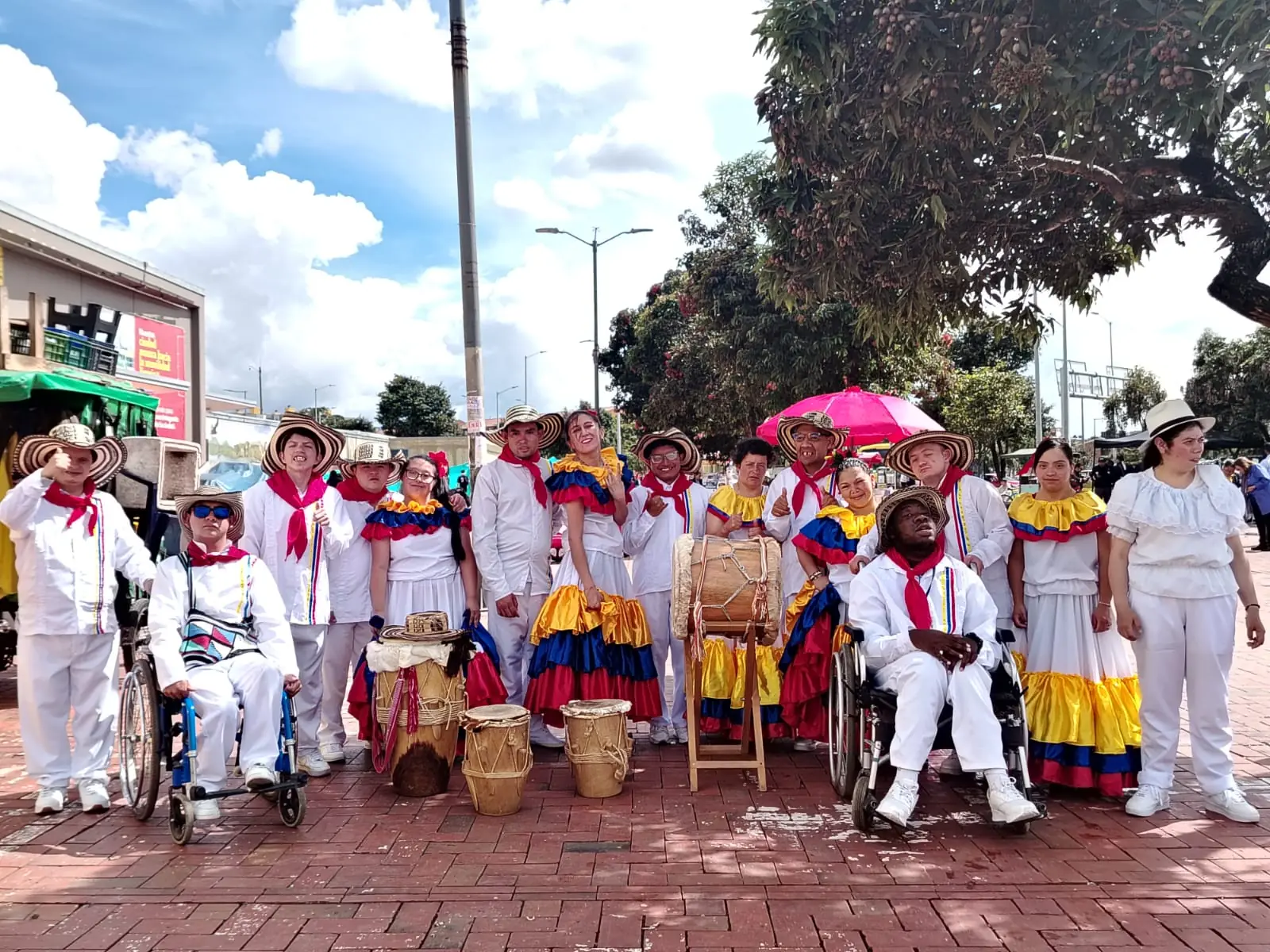 Grupo de gaitas y tambores con vestuario blanco, pañoleta roja y polleras de colores posando en una plaza