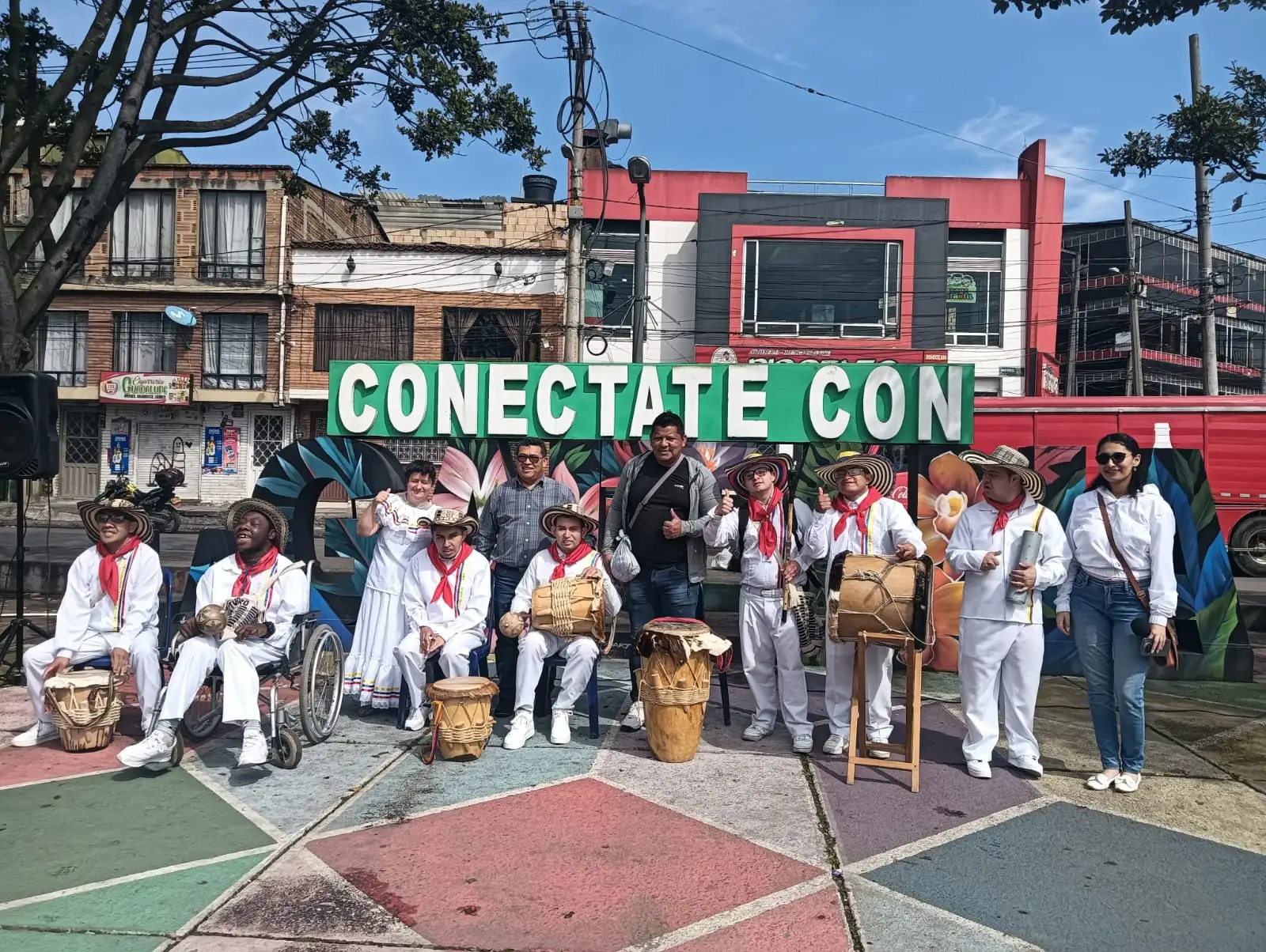 Nuestros artistas con vestuario blanco, pañoleta roja y sombrero vueltiao, junto a sus tambores en una plaza